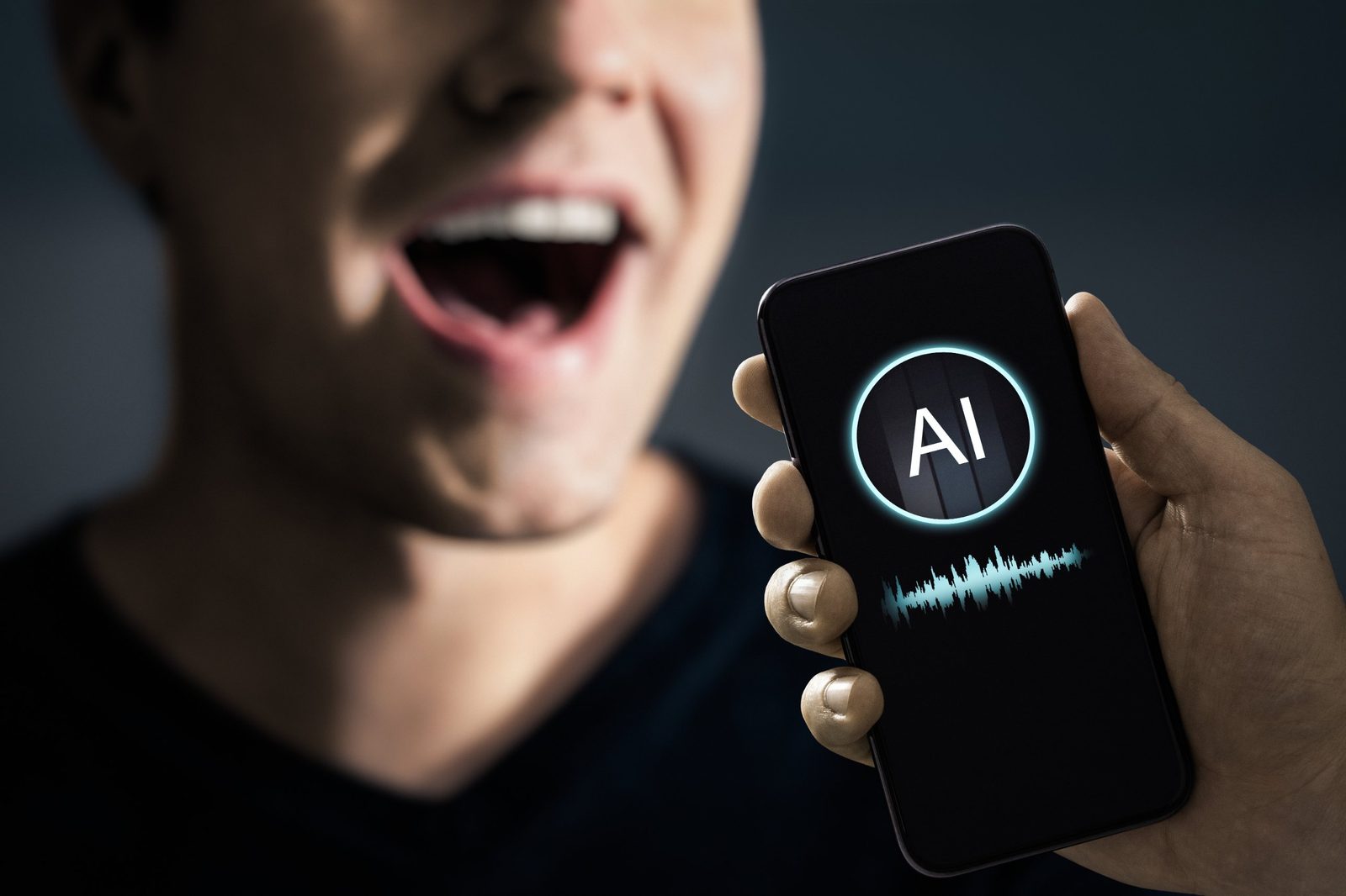 Smartphone showing an AI icon and sound waveform held up to a person speaking, representing synthetic voice and voice cloning